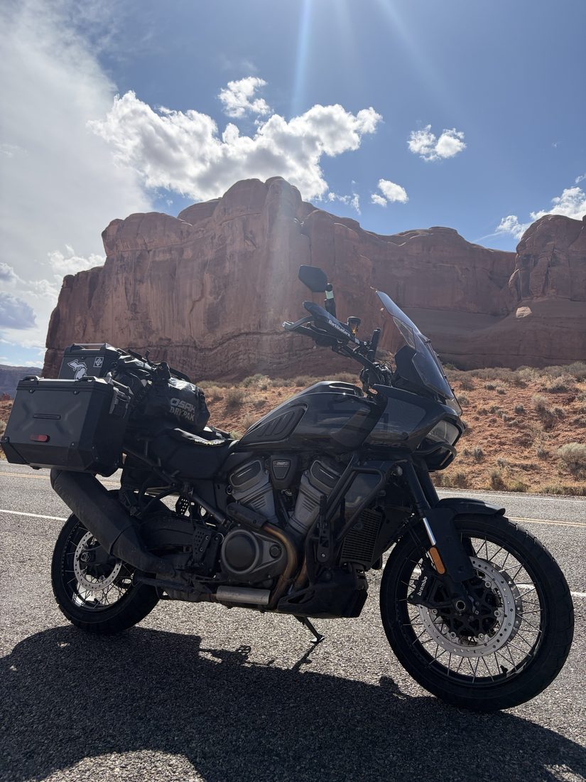 Ron's adventure bike loaded with luggage, parked on a desert road in front of red rock cliffs