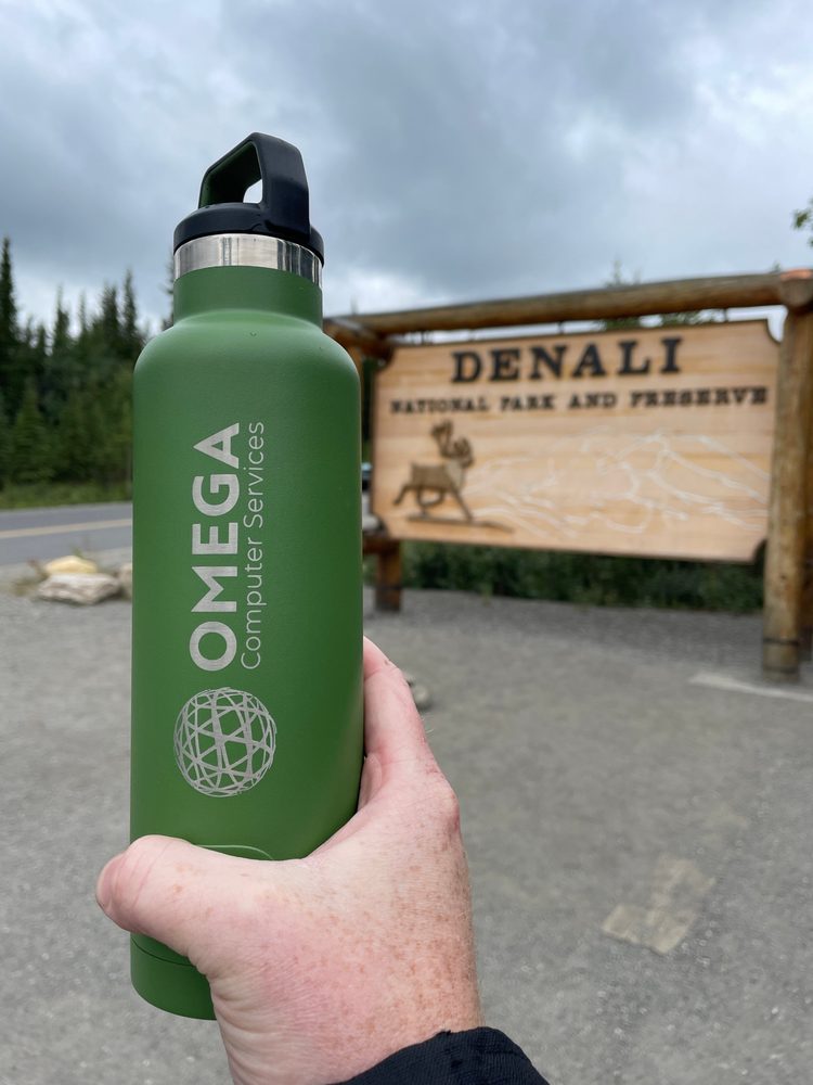 The green Omega water bottle held up in front of the Denali National Park entrance sign